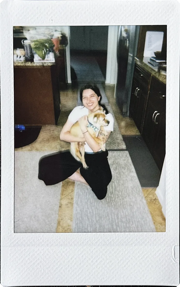 Instant photo of Abby sitting on a kitchen floor, hugging a small rescue dog