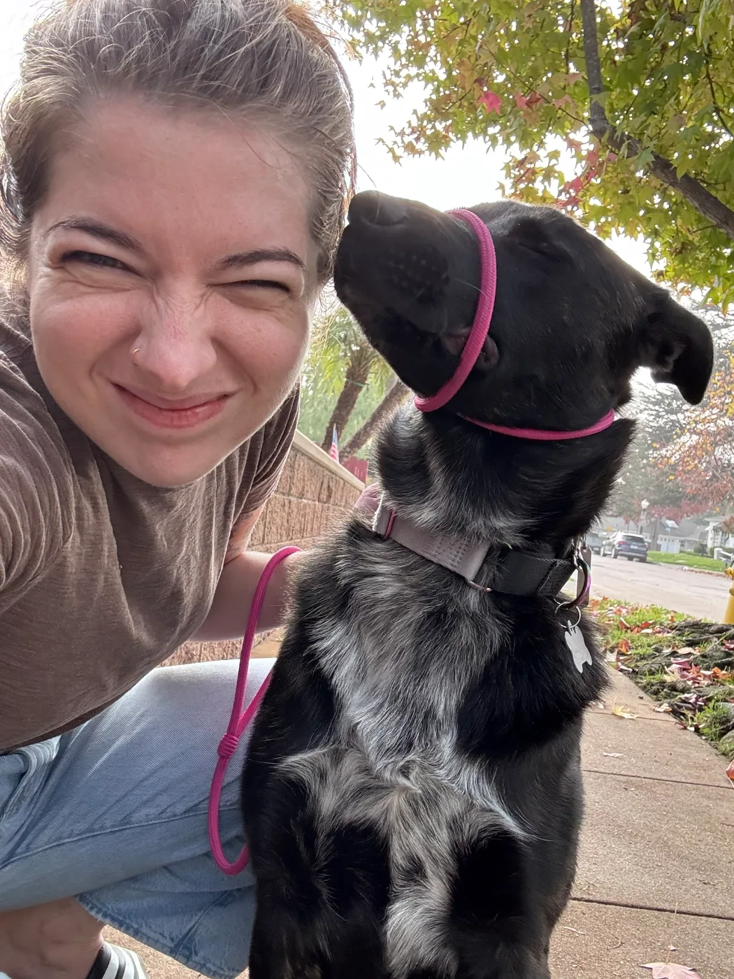 Abby squinting into a selfie beside a black dog on a pink leash